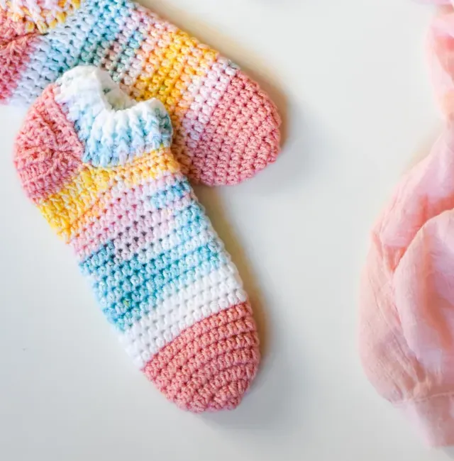 A pair of pastel rainbow-striped crochet ankle socks on a white surface